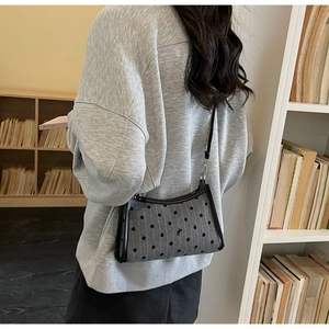 Polka dot underarm bag with black bow and leather trim worn by model in a library