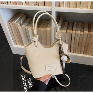 Detail of cream bucket bag with textured leather, top handle, and baseball glove charm accessory