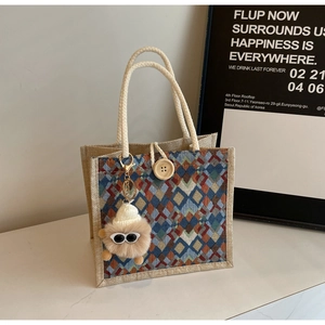 Detail of rhombic woven tote bag featuring thick rope handles and a plush monster charm