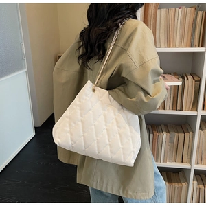 Detail of white quilted tote bag with golden chain strap worn by a model in a library