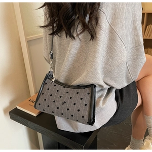 Detail of grey polka dot underarm bag with black leather straps on a model