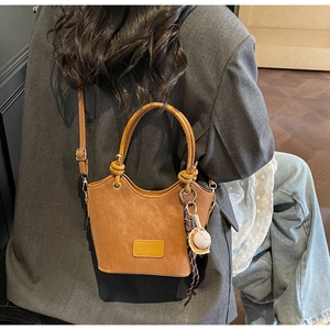 Detail of caramel leather bucket bag with white baseball pendant and woven rope charm
