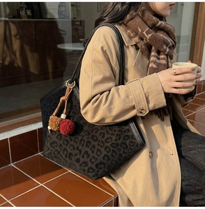 Detail of leopard print tote bag with plush pompom charm and black leather straps