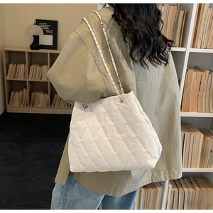Detail view of large white quilted tote bag featuring golden hardware and chain straps