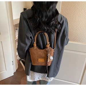 Brown frosted leather bucket bag featuring baseball charm and woven strap detail