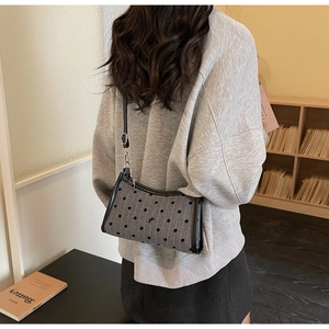 Polka dot underarm bag with bow detail shown on shoulder in a cozy interior scene