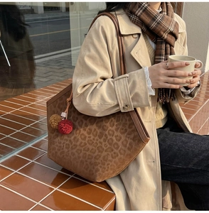 Detail of leopard print tote bag with plush pom-pom charms and smooth faux suede texture