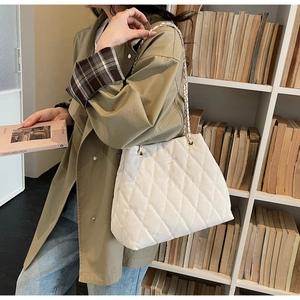 Detail of white quilted tote bag with gold chain strap shown on a model in a library