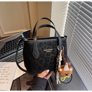 Detail of black leopard embossed tote bag with gold logo and bear charm on desk