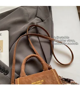Detail of a brown leather mini bag with adjustable shoulder strap and gold lettering