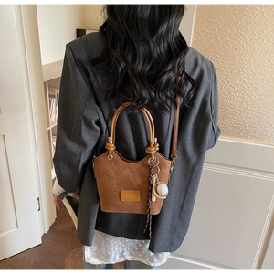 Brown suede bucket bag with round handle and tassel detail shown in casual street style outfit