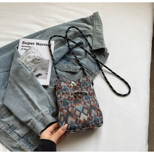 Vue à plat d'un sac à bandoulière tissé à motifs géométriques sur une veste en jean bleu