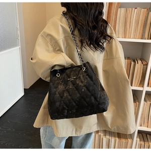 Detail of black quilted tote bag featuring leather-woven metal chain and logo lettering