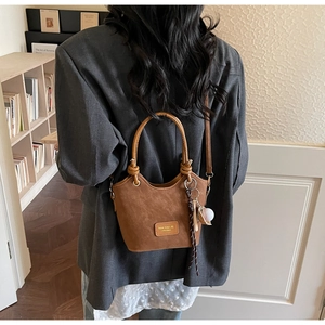 Brown bucket bag with round handle and baseball charm shown on a model in a cozy room