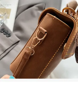 Close-up of golden hardware clasp and yellow stitching on a brown leather shoulder bag