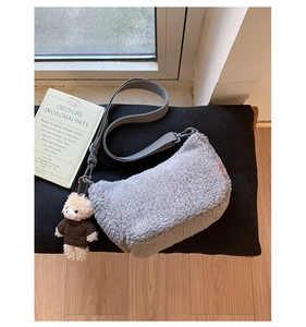 Détail d'un sac bandoulière en peluche grise avec pendentif ours et bandoulière en tissu