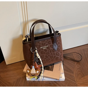 Detail of leopard print tote bag with adjustable strap and decorative charms on books