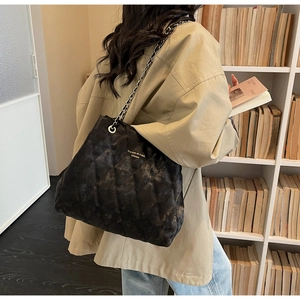 Detail of black quilted tote bag featuring leather-woven chain strap in a library setting