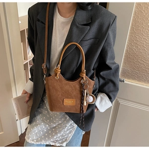 Detailed view of a vintage brown leather bucket bag with retro sports charms and brand tag