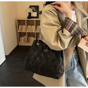 Detail of black quilted shoulder bag featuring silver chain strap and velvet texture