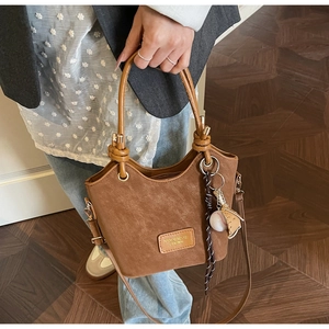 Detail of brown bucket bag featuring knotted handles and a baseball-themed charm pendant