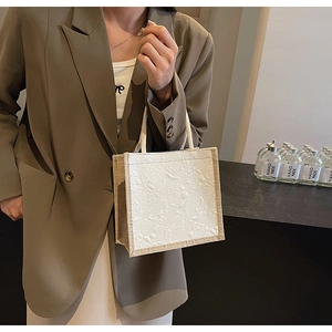 Detail of cream floral embossed tote bag with woven handles and contrasting canvas trim