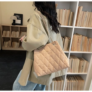 Detail of beige quilted tote bag with metal chain strap in a lifestyle library setting