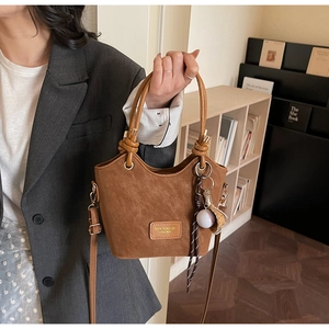 Detailed shot of brown suede bucket bag with leather brand patch and baseball charm