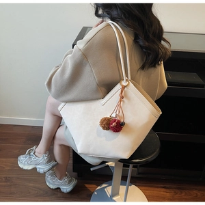 Detail of cream large tote bag with V-shaped edge and colorful pompom charms on shoulder strap