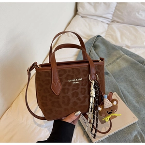 Detail view of leopard print tote bag with plush bear charm and woven tassel accessories