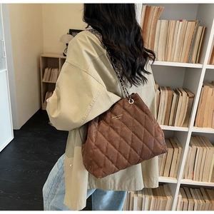 Detail of brown quilted tote bag with gold logo and leather-chain strap in a cozy setting