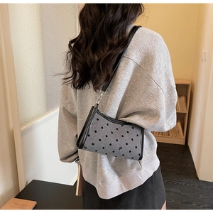 Detailed view of grey polka dot underarm bag with bow embroidery worn by a model