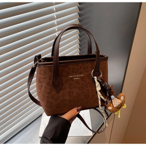 Detail of dark brown leopard print tote bag with teddy bear charm and gold logo