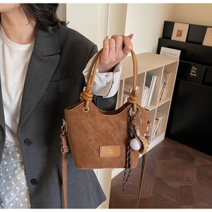 Close-up of brown suede bucket bag with round handles and baseball charm ornament