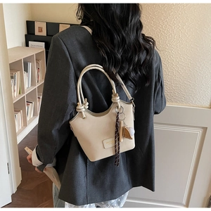 Detail of beige bucket bag with knotted handle and plush charm on a model in a grey suit
