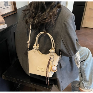 Close-up of cream bucket bag featuring brand label and stylish baseball charm detail