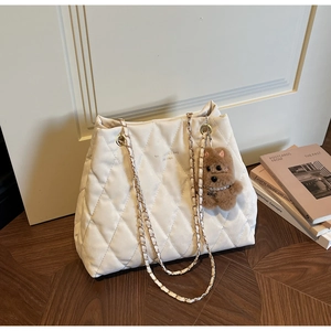 Detail of white quilted tote bag with metal chain strap and cute plush dog pendant