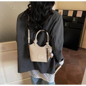Detail of beige minimalist bucket bag with round handle and baseball charm on shoulder strap