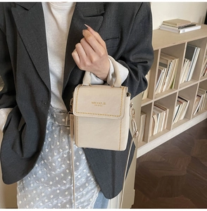 Detail of beige square handbag with gold studs and brand logo in an elegant urban setting