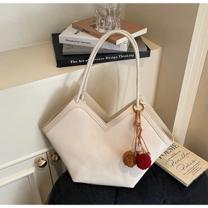 Close-up of cream tote bag featuring a V-shaped top cut and plush pompom charm detail