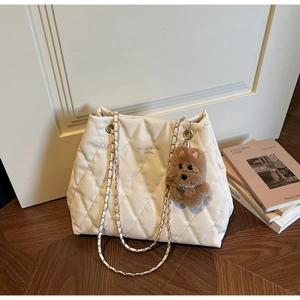 Detail of white quilted tote bag with gold chain strap and brown plush puppy charm