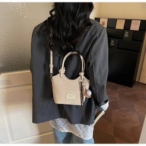Beige bucket bag with top handle and shoulder strap shown on a model in a blazer