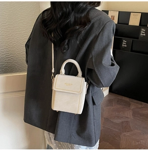 Detail of a minimalist cream-colored mini leather handbag with gold accents on grey suit