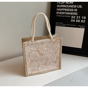 Detail of beige woven handbag featuring 3D rose embroidery and rope handle texture