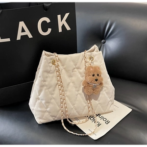Close-up of cream quilted tote bag with gold chain strap and cute brown teddy bear charm