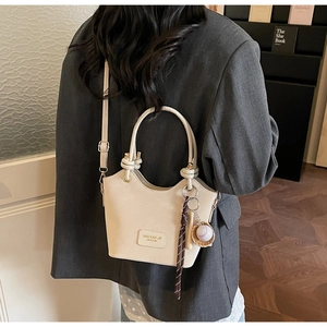 Detail view of cream bucket bag with baseball charm on a grey blazer outfit