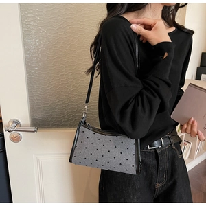 Close-up of grey underarm bag with black heart patterns and shiny leather straps on model