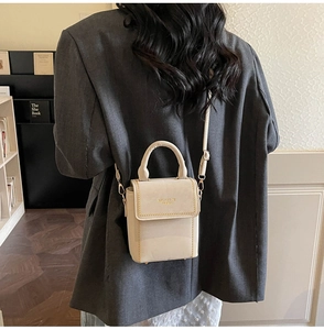 Detail of cream mini crossbody bag with gold chain trim and handle on grey blazer