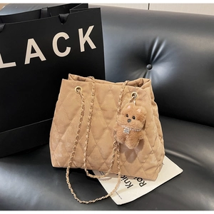 Detail of khaki quilted tote bag with chain strap and small teddy bear charm accessory