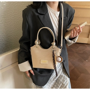 Detail of beige PU leather bucket bag featuring a knot handle and baseball charm